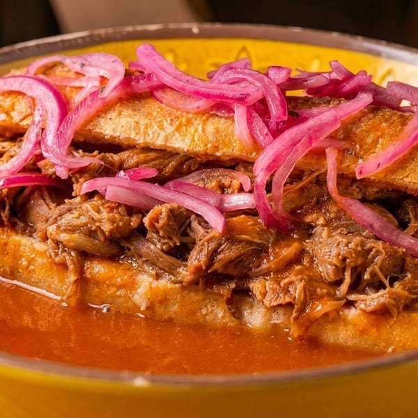 A torta ahogada, a Mexican sandwich, filled with shredded meat and topped with pickled red onions.
