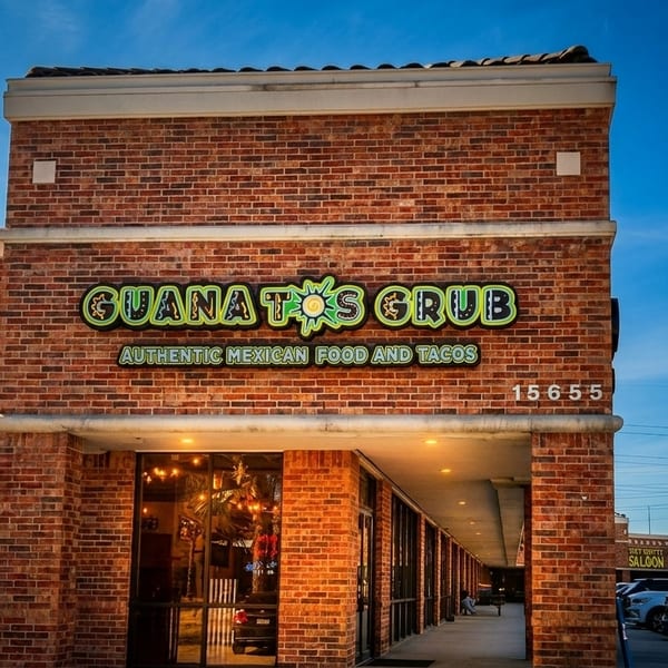 Exterior of Guanatos Grub restaurant with a brick facade, large windows, and a bright sign.