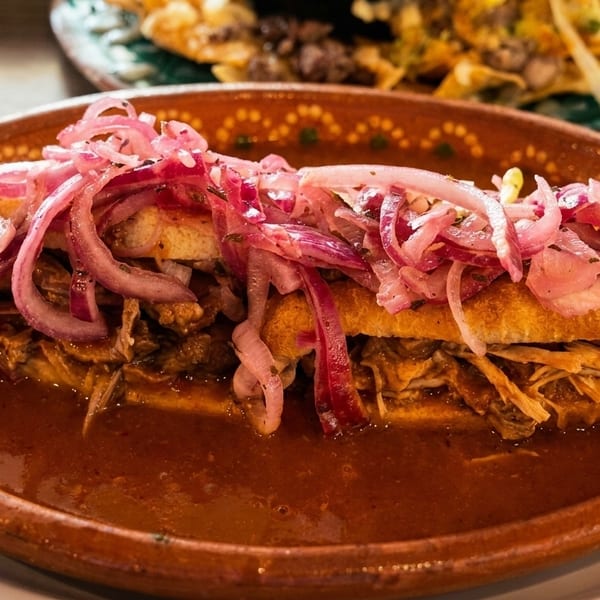 A torta ahogada, a Mexican sandwich drowned in red sauce and topped with pickled red onions.