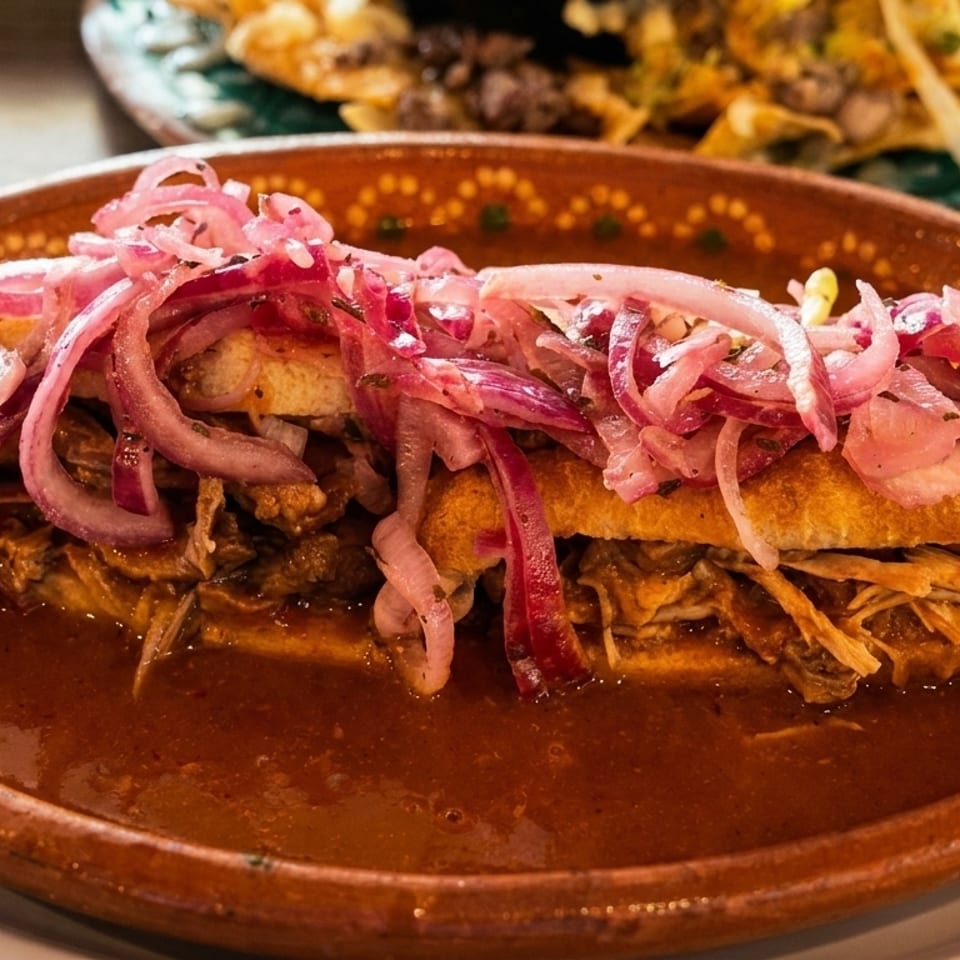 A torta ahogada, a Mexican sandwich drowned in red sauce and topped with pickled red onions.