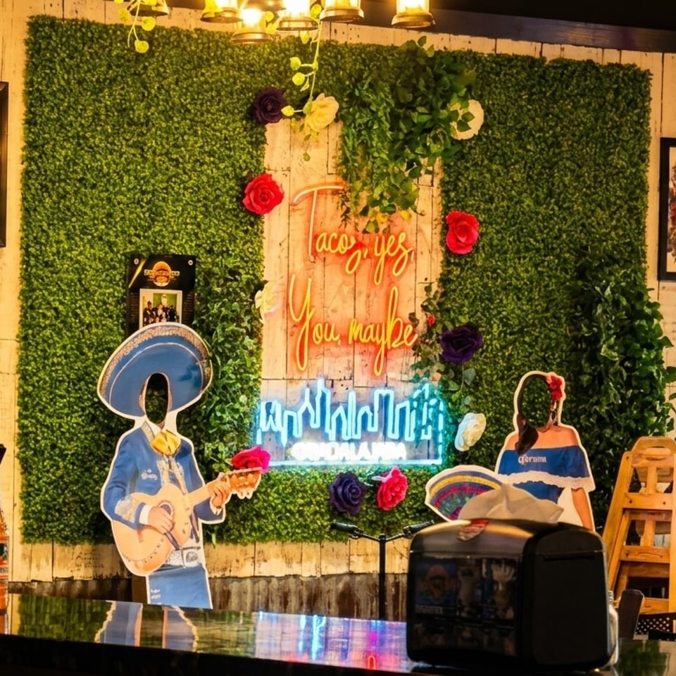 A vibrant restaurant interior with a neon "Taco yes, You maybe" sign on a green wall.